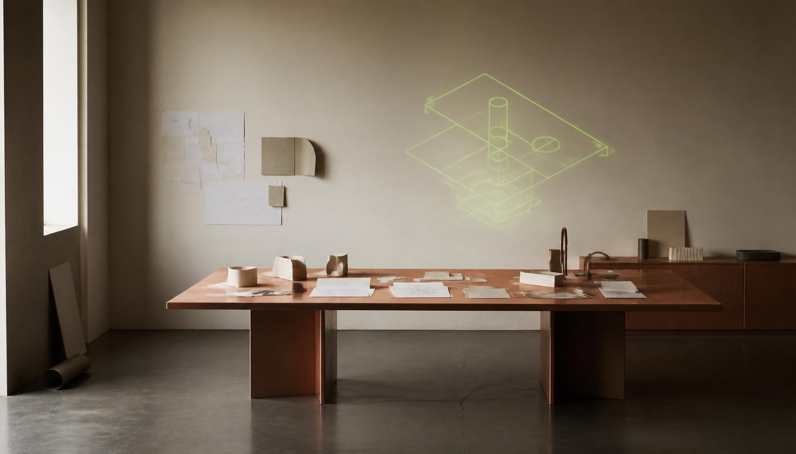 Editorial workspace — copper worktable with paper prototypes and a lime wireframe projected on a bone wall.